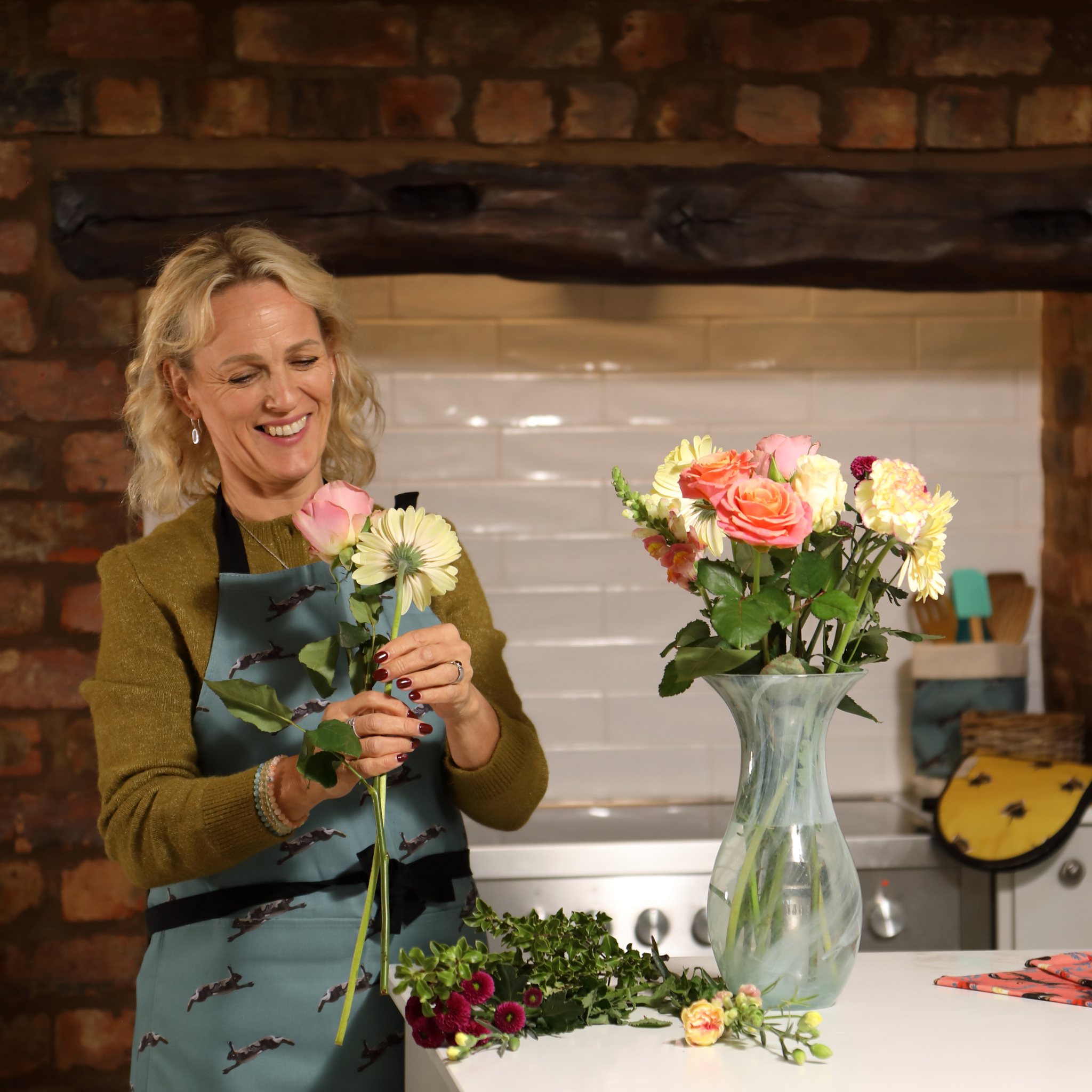 Woman arranging flowers in a kitchen with a brick wall background