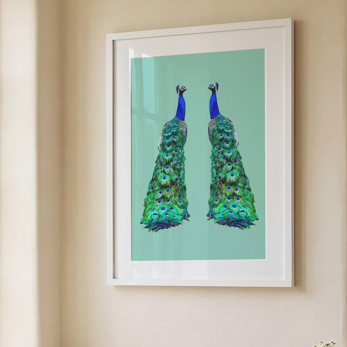 A framed art print featuring two peacocks with vibrant green and blue feathers on a light teal background, hung on a beige wall.