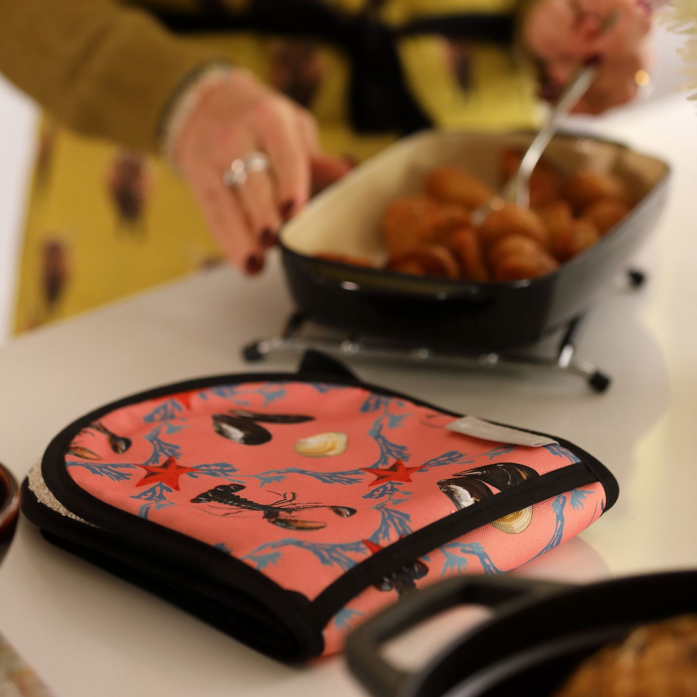 Person cooking food in a pan with a pink pot holder featuring lobster designs.