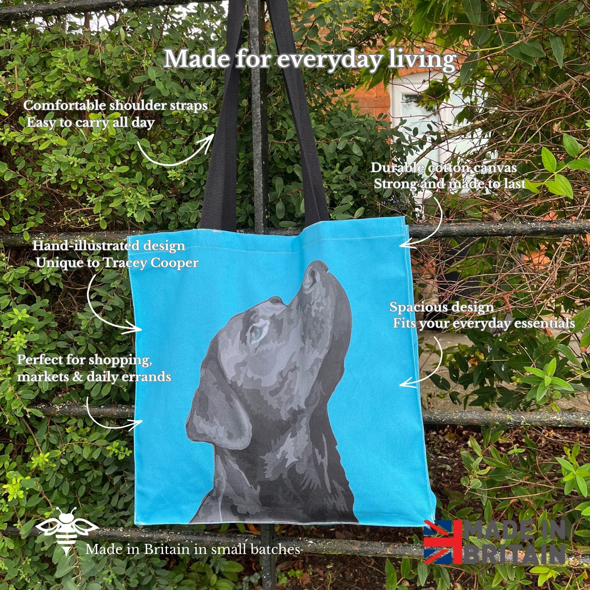 Blue tote bag with a dog illustration on a metal fence with greenery.