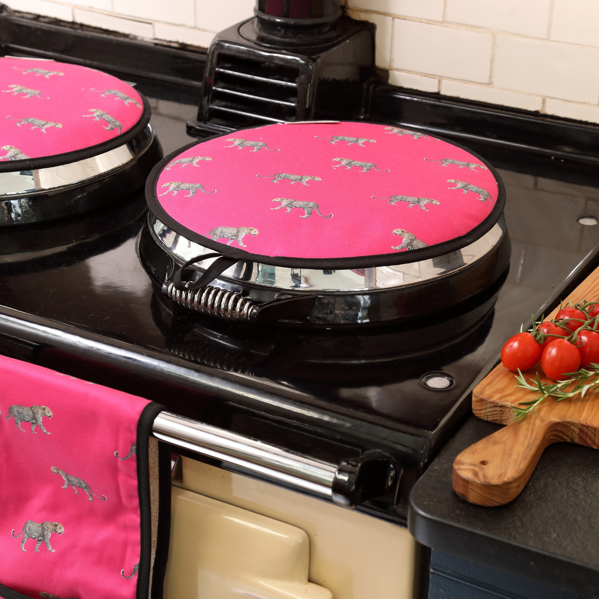 Bright pink AGA covers with a leopard print, shown on a black vintage Aga stove in a kitchen setting.