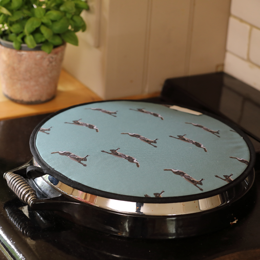 A brown hob cover with a pattern of hares running, placed on a stovetop.