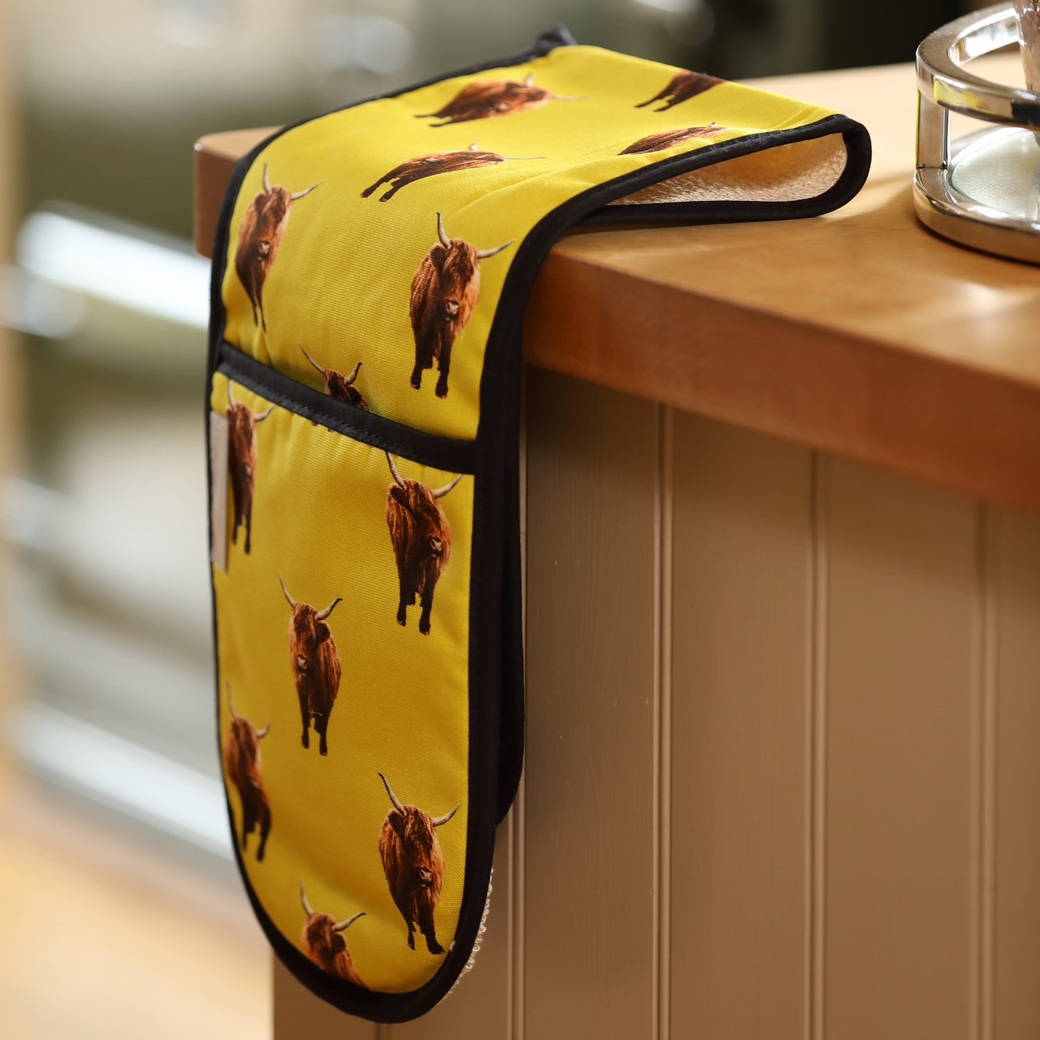 A mustard yellow highland cow oven glove in rustic kitchen