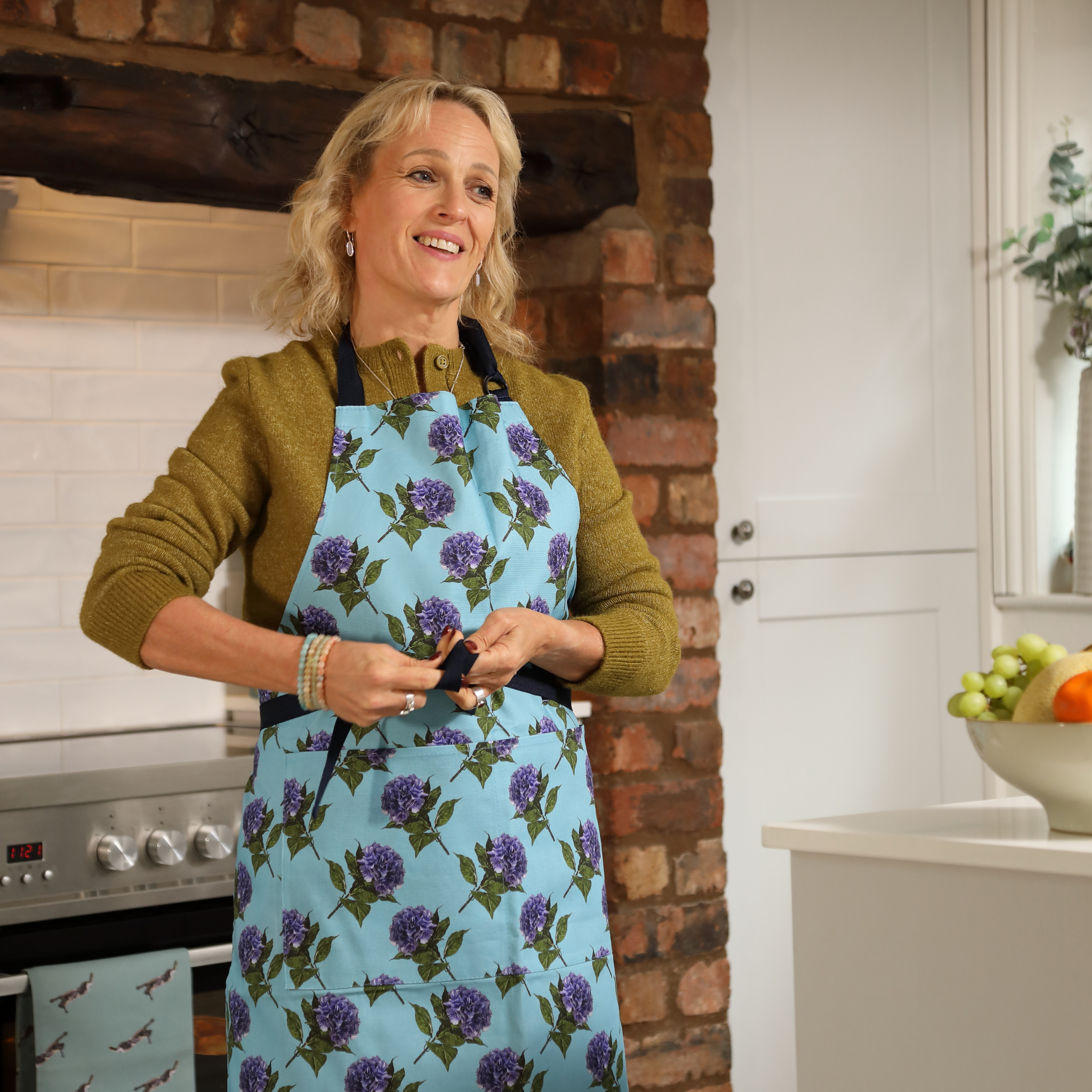 Woman wearing a blue apron with purple floral pattern in a kitchen.