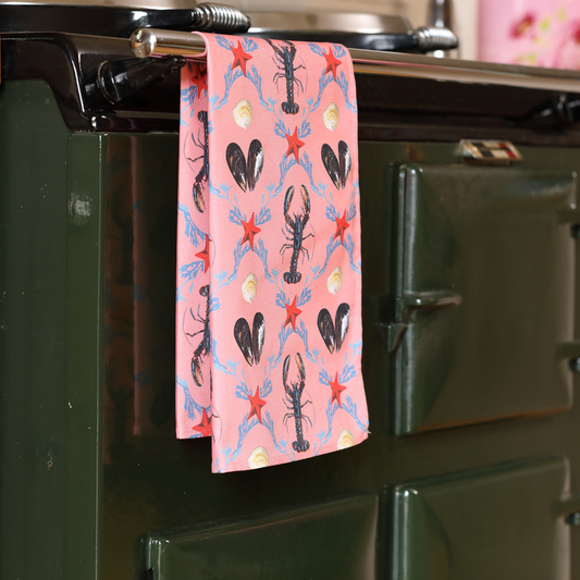 Hand-illustrated Lobster Tea Towel by Tracey Cooper — 100% cotton, printed in the UK, featuring a playful lobster and mussels on salmon pink.