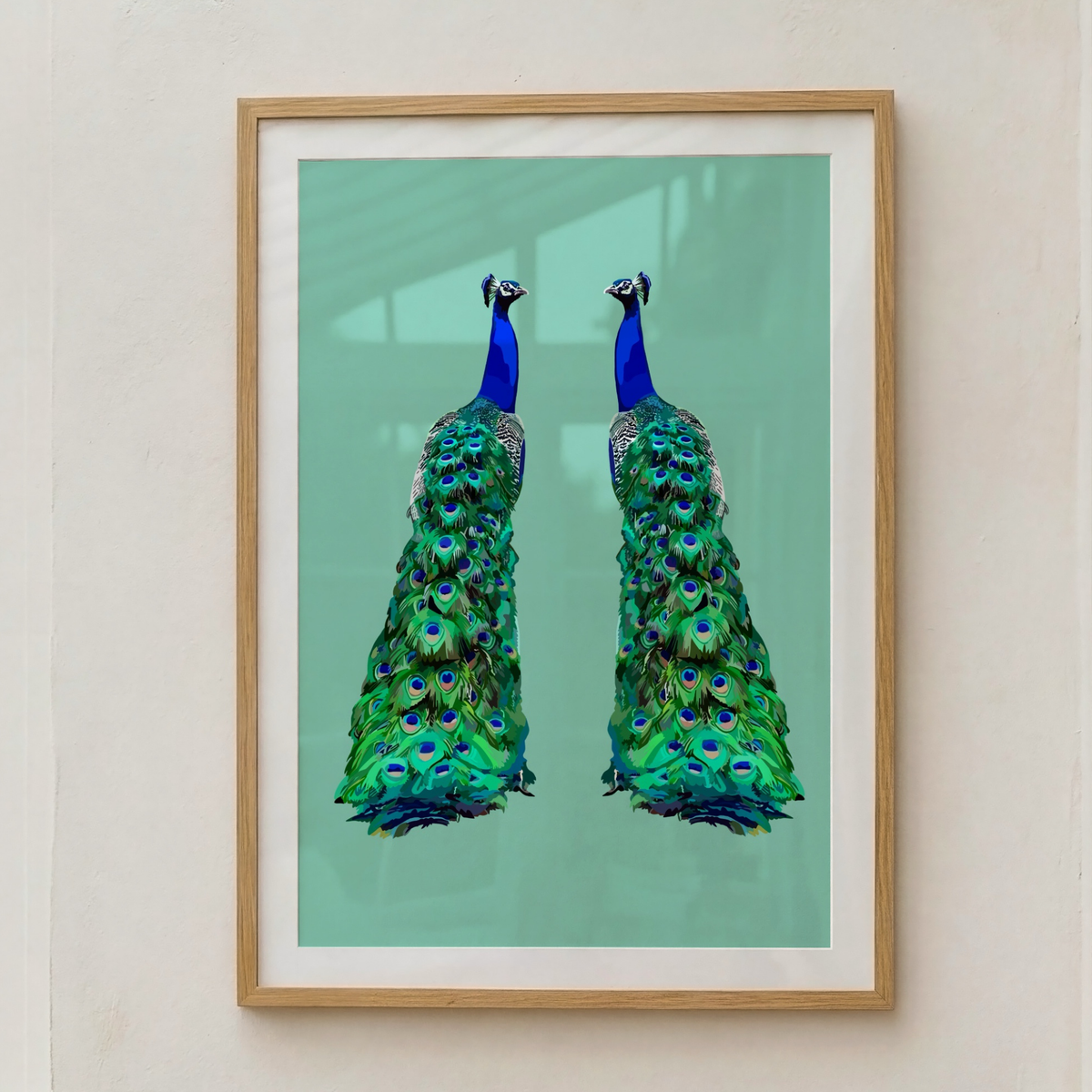Framed wall art featuring two mirrored peacock birds on a mint green background, hung on a light beige wall.