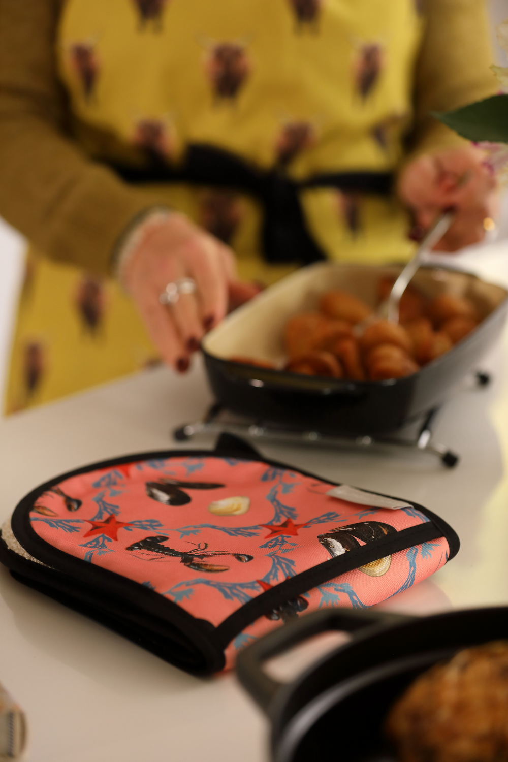 Person holding a bowl of food with a pink pot holder featuring lobster designs on a table.