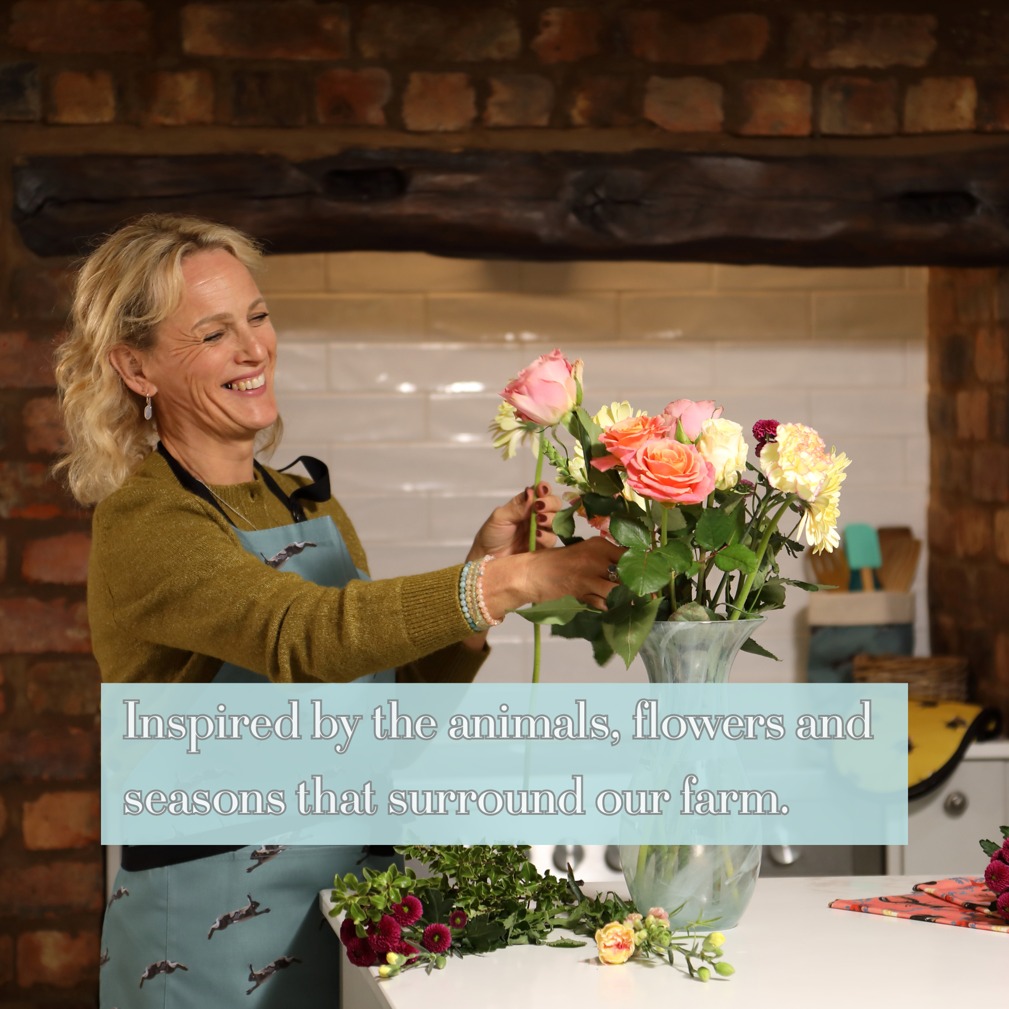 Tracey Cooper arranging flowers in a country kitchen wearing a hand-illustrated apron inspired by her farm