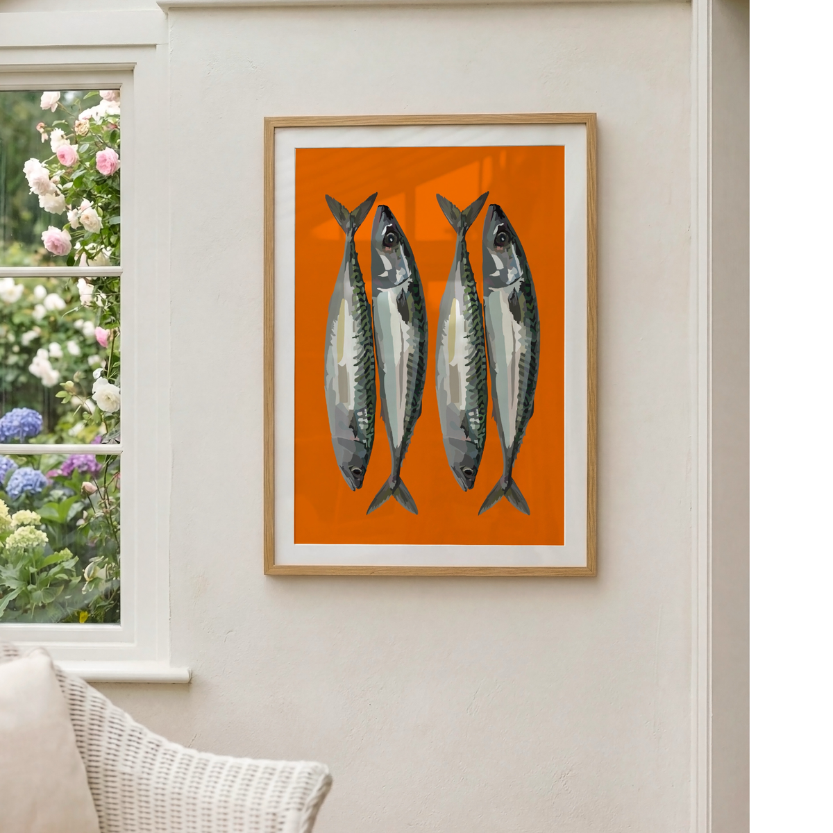 Framed wall art featuring four silver fish on a bright orange background, hung on a light beige wall next to a window with flowers visible outside.